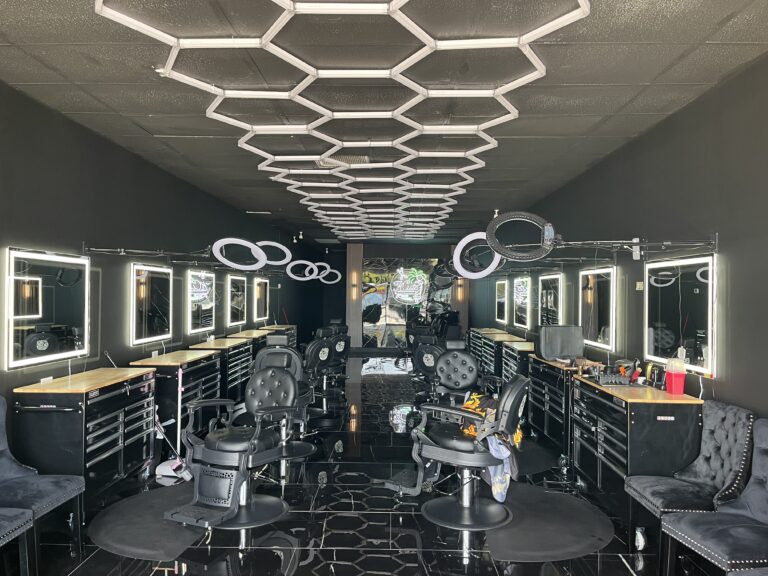 Modern barbershop interior with illuminated mirrors and styling chairs.